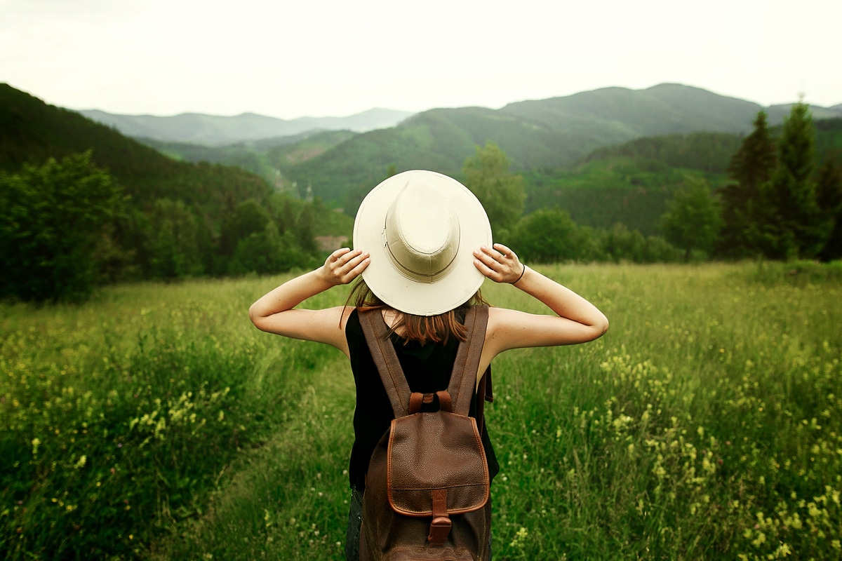 Jeune femme marchant dans un champ vert avec un chapeau et sac à dos