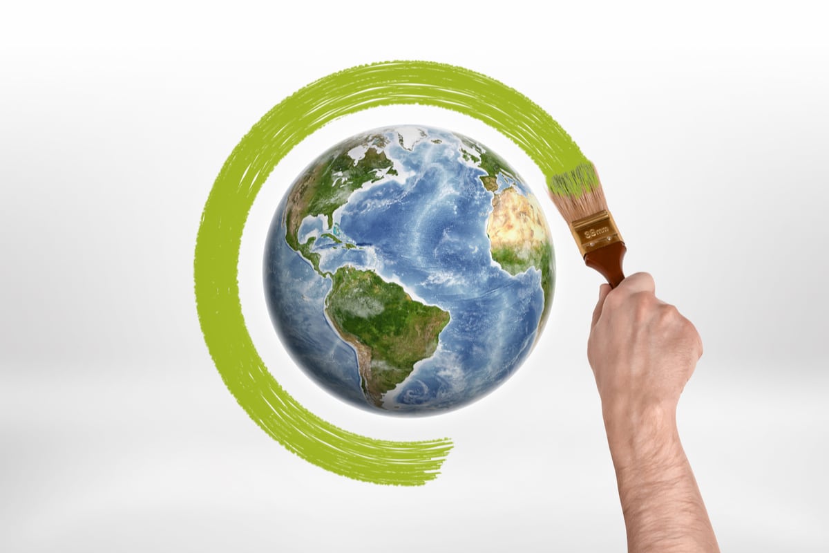 Main tenant un pinceau, entourrant de vert un dessin de la planète Terre