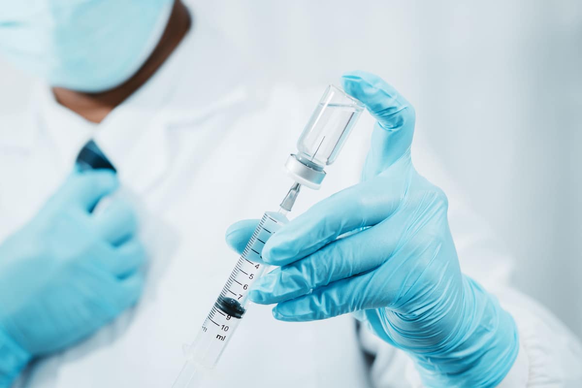 Médecin avec des gants bleus tient une seringue et un flacon de vaccin