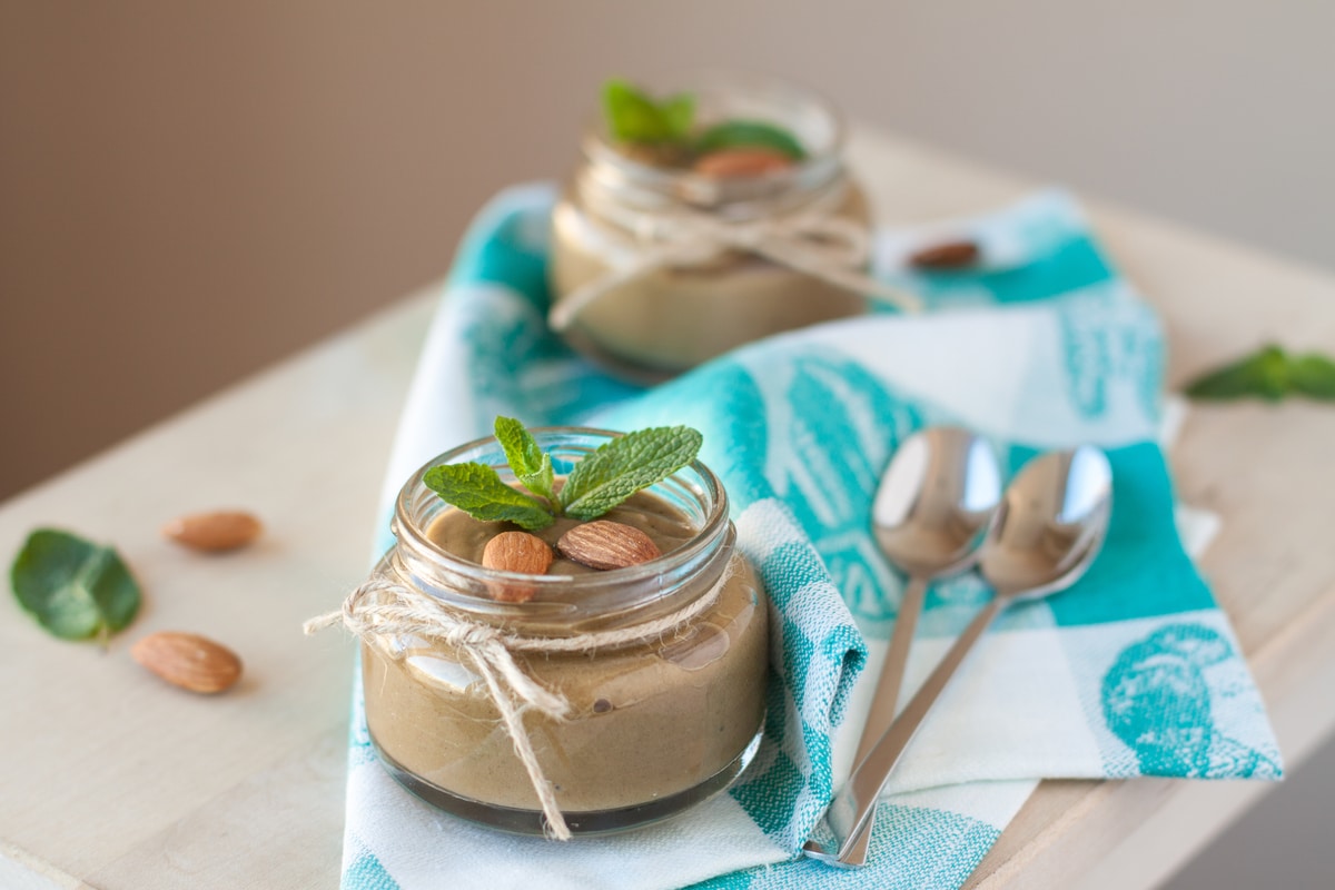 Purée d'amande dans un pot en verre, feuilles de manthe, amande entière et cuillère