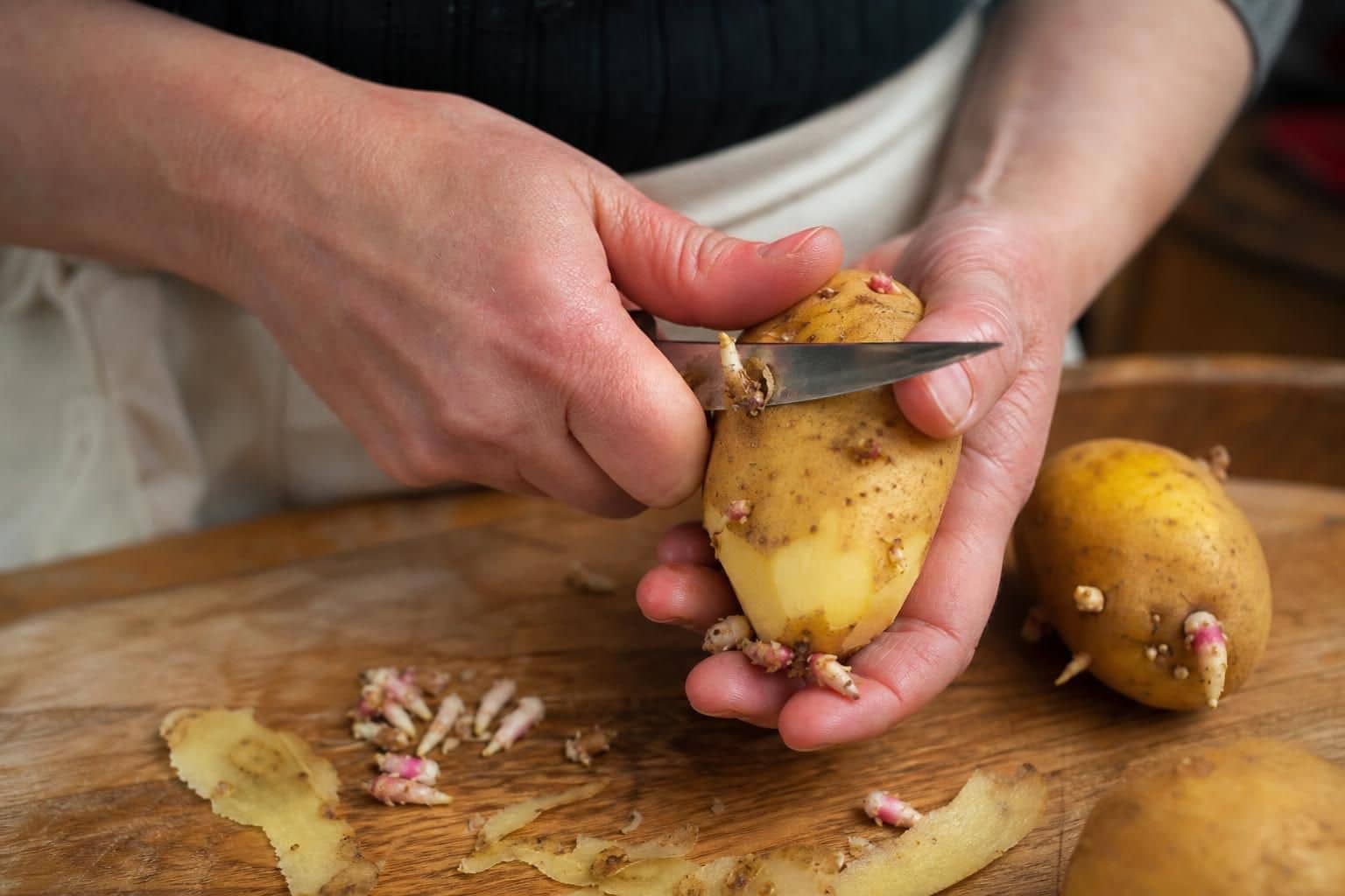 Main retirant les yeux d une pomme de terre sur planche en bois